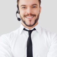Confident male operator. Handsome young man in formalwear and headset looking at camera and smiling while standing against grey background